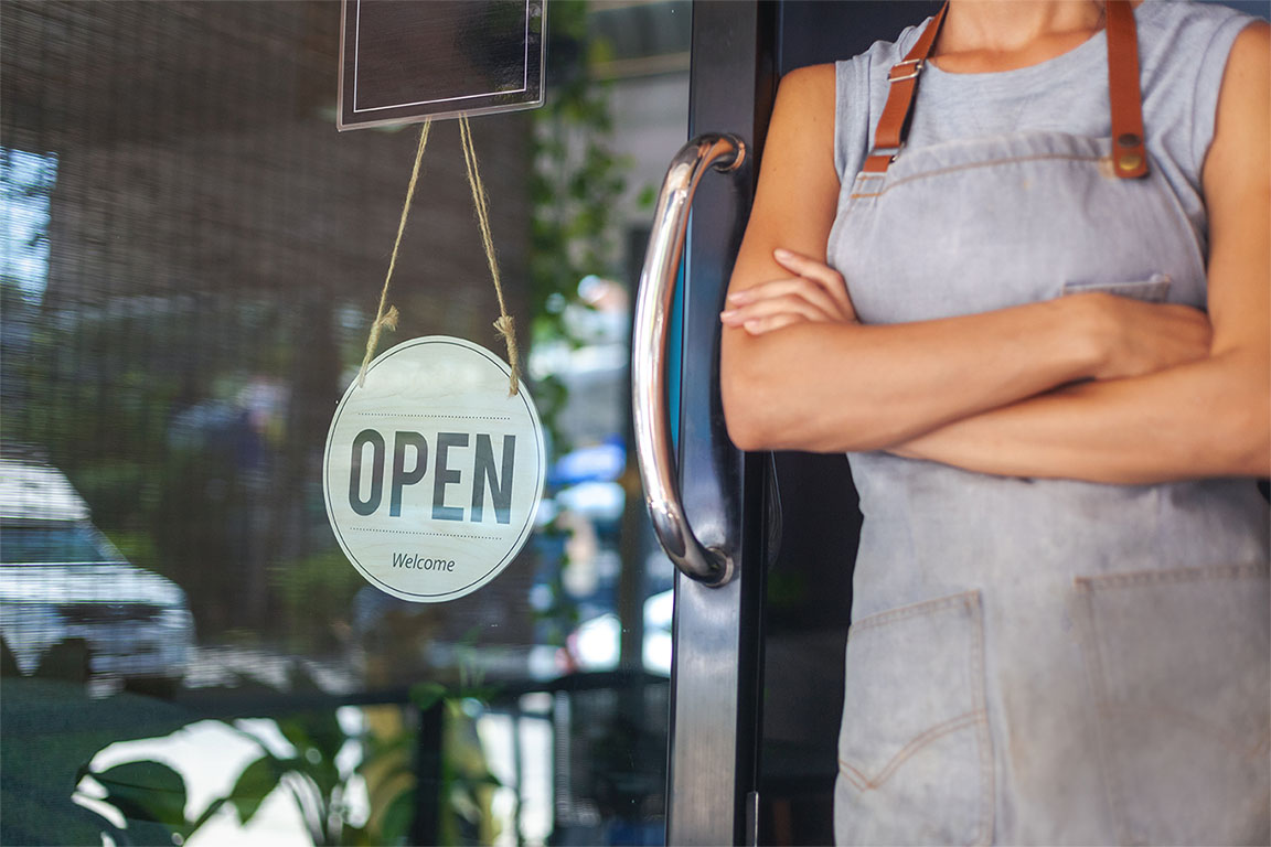 Image of a person leant up against a glass door to a cafe with an 'open' sign displayed to support future of small business article
