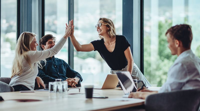 Image of a group of business professionals sat round a large desk smiling and high-fiving to support skills for success article