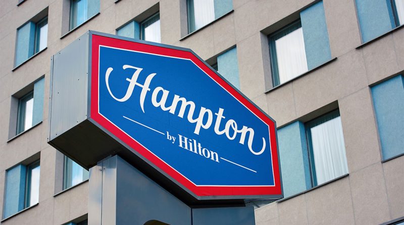 Image of a sign on the side of a building displaying the Hampton by Hilton logo in red, white and blue to support business success article