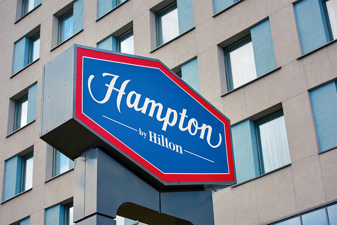 Image of a sign on the side of a building displaying the Hampton by Hilton logo in red, white and blue to support business success article