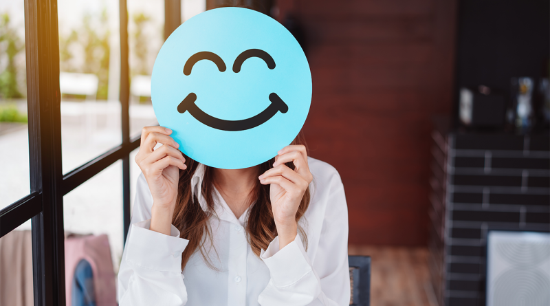 Image of a woman in a professional work setting holding a smiley face icon in front of her face to support good employee article