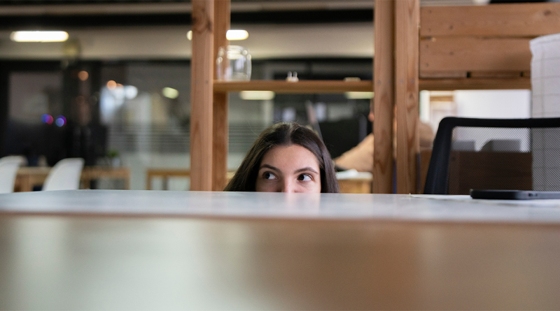 Image of woman peeking out from behind desk to support stealth mode startup strategy article