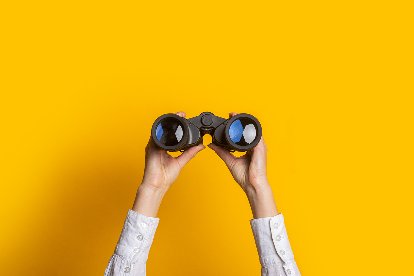 Person holding up binoculars against a yellow background to support talent shortage article