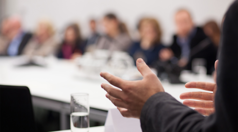 Executive presenting a strategy during a boardroom meeting with business leaders seated around a conference table.